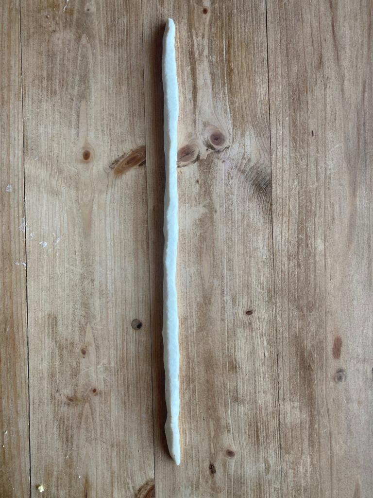 a long rope of sourdough pretzel dough on a wooden countertop