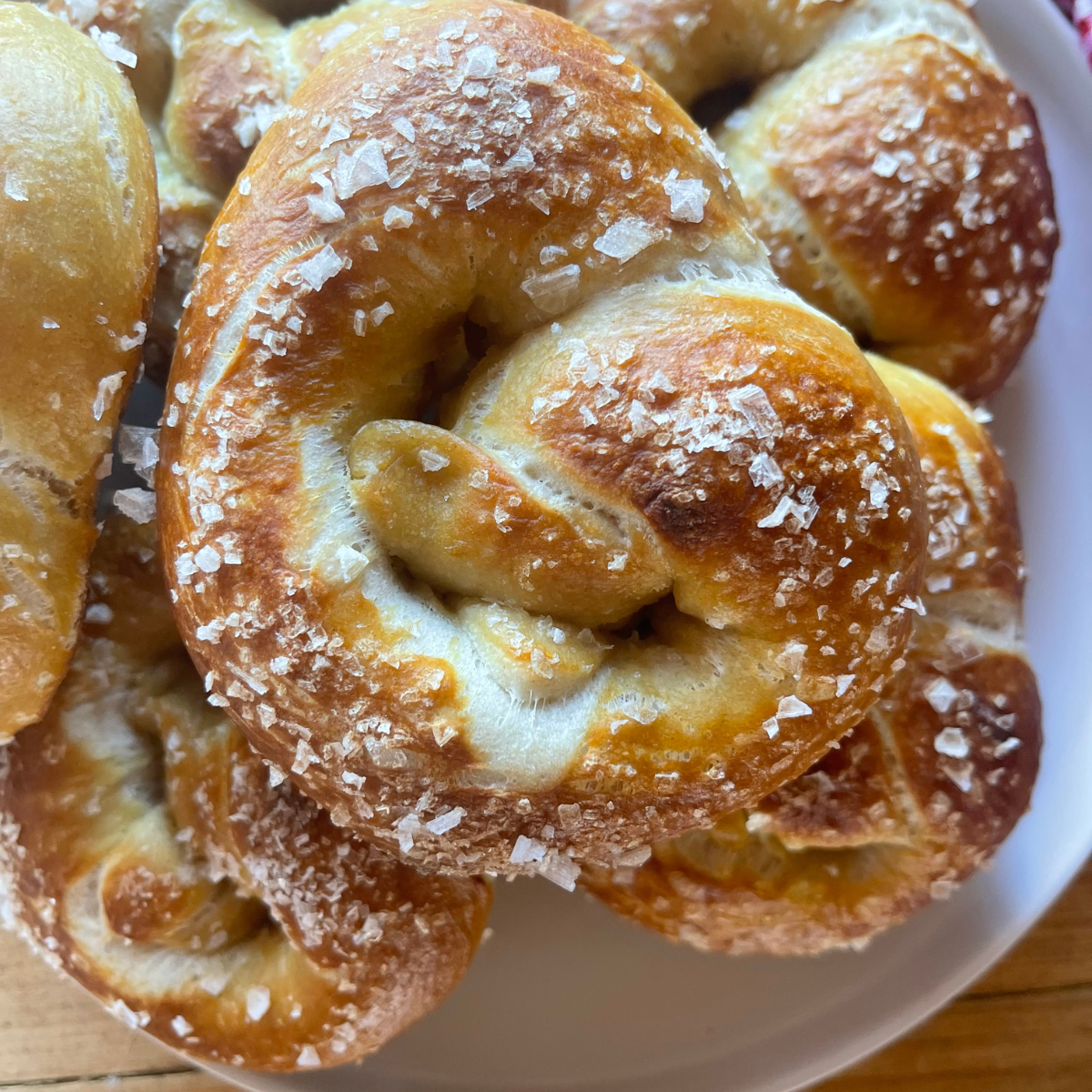 a stack of sourdough soft pretzels on a white plate, each baked until golden brown and topped with coarse salt