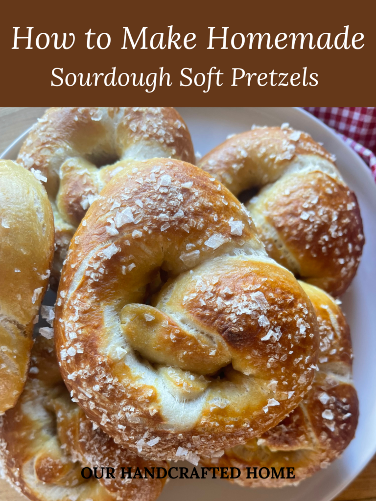 a stack of sourdough soft pretzels on a white plate, each baked until golden brown and topped with coarse salt. Text overlay reads "How to Make Homemade Sourdough Soft Pretzels"