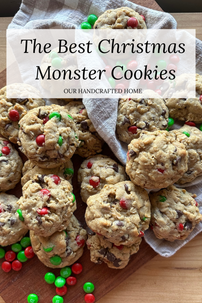 Christmas monster cookies piled on a wooden board, packed with oats, chocolate chips, and red and green M&M candies for a festive holiday treat. Text overlay reads "The Best Christmas Monster Cookies."