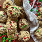 Christmas monster cookies piled on a wooden board, packed with oats, chocolate chips, and red and green M&M candies for a festive holiday treat.