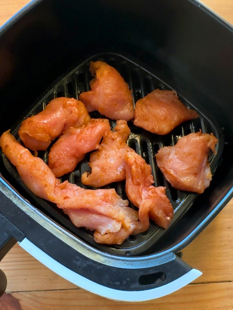 seasoned uncooked chicken breast arranged in the bottom of an airfryer