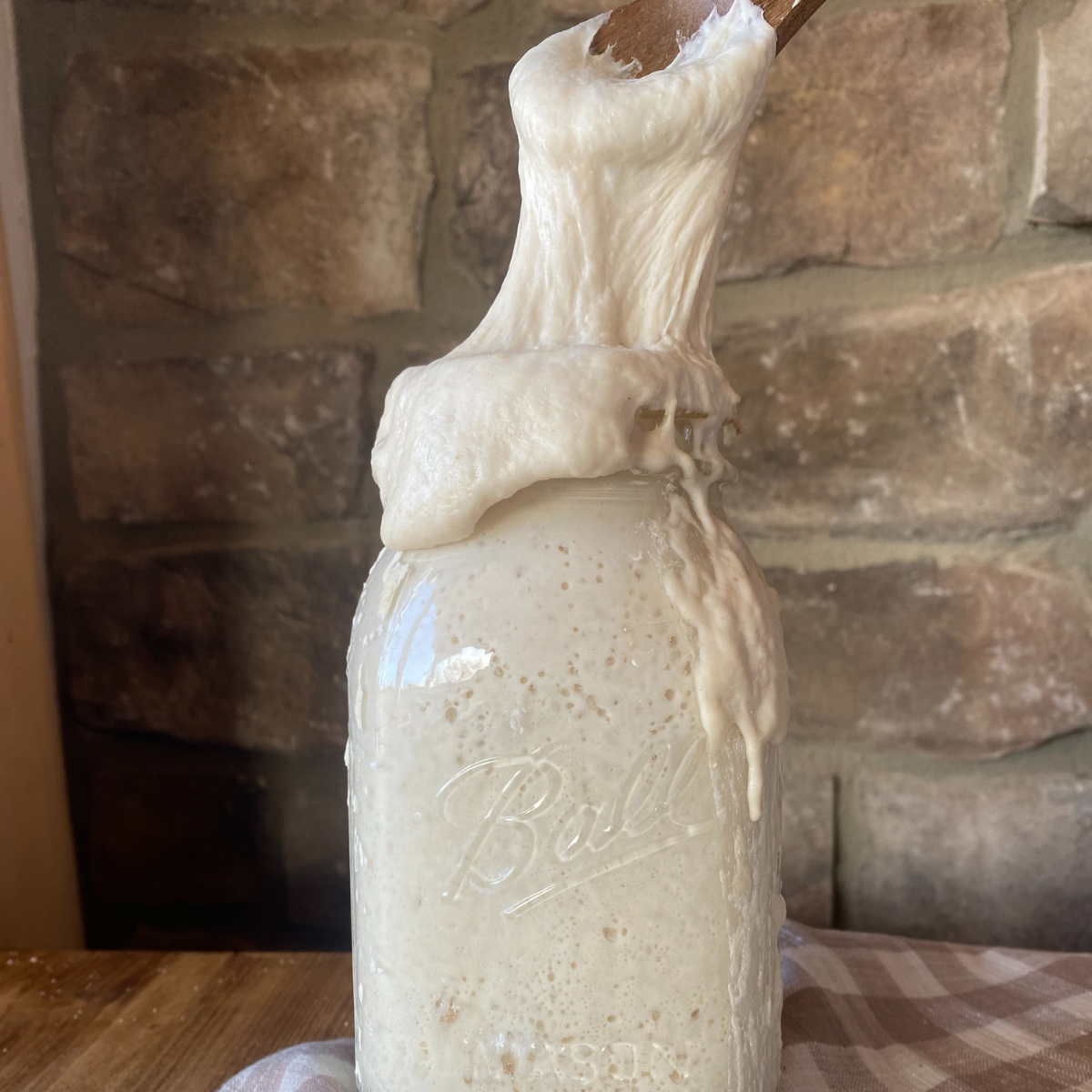 a jar of sourdough starter, with a spoon inserted into the middle, pulling some of the starter away from the jar