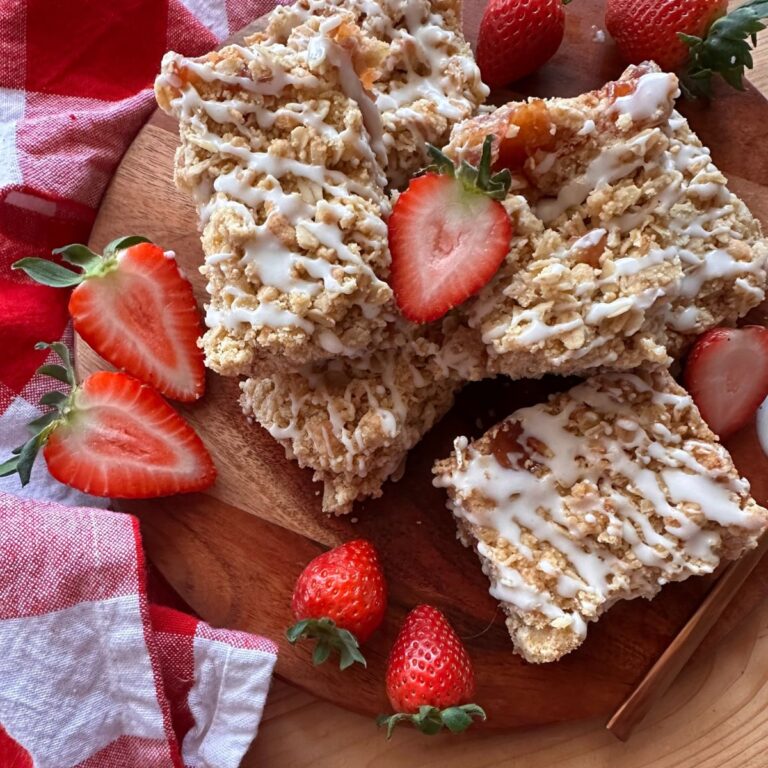 a close up view of strawberry oatmeal bars cut into squares and drizzled with vanilla icing. Sliced strawberries are arranged around the top and perimeter of the bars