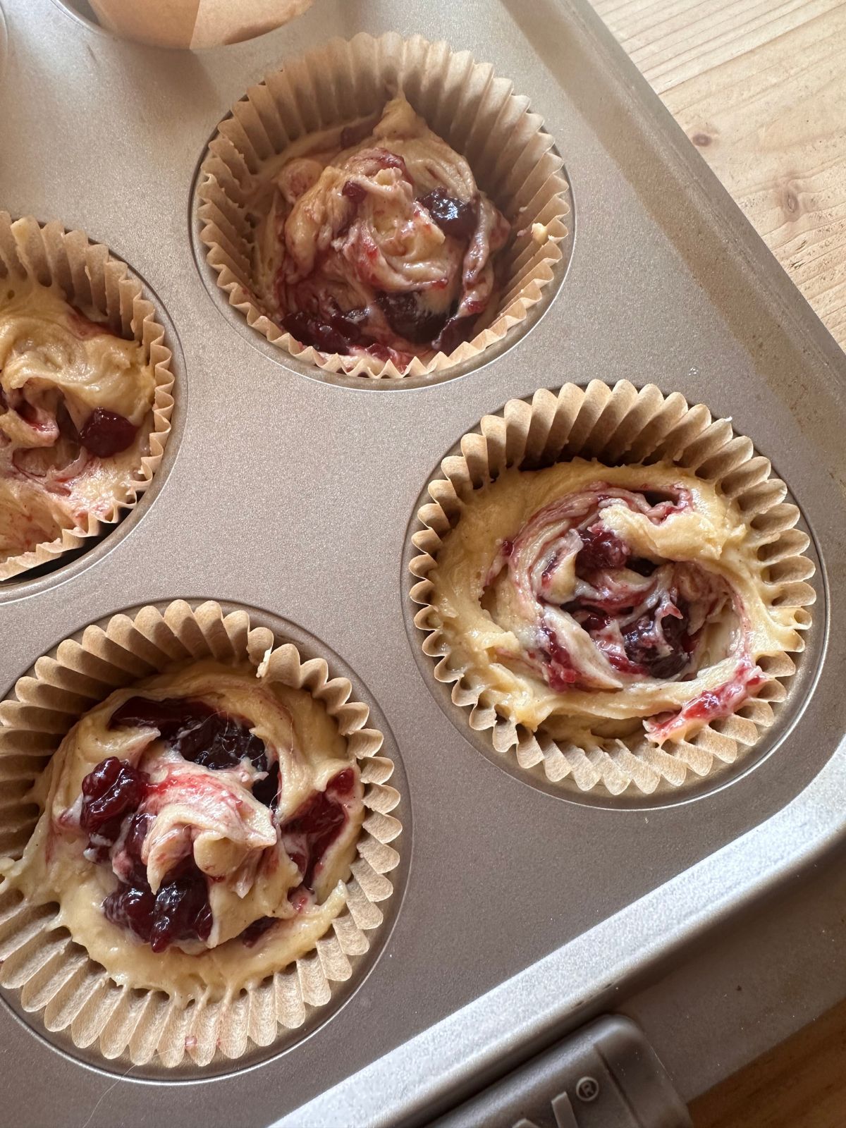 blackberry muffin batter sits in a muffin tin, with blackberry jam swirled into the middle of each muffin