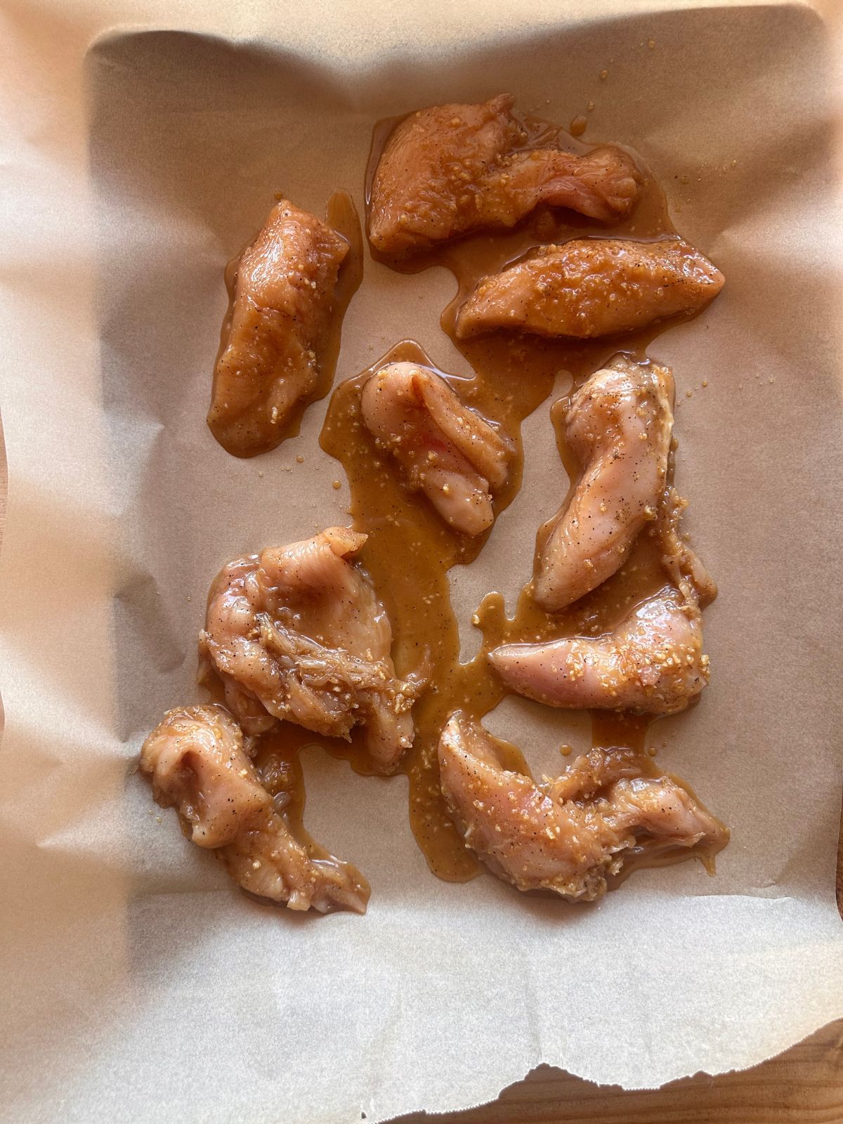 unbaked chicken tenders tossed in a honey garlic sauce, spread out on a parchment paper lined baking sheet