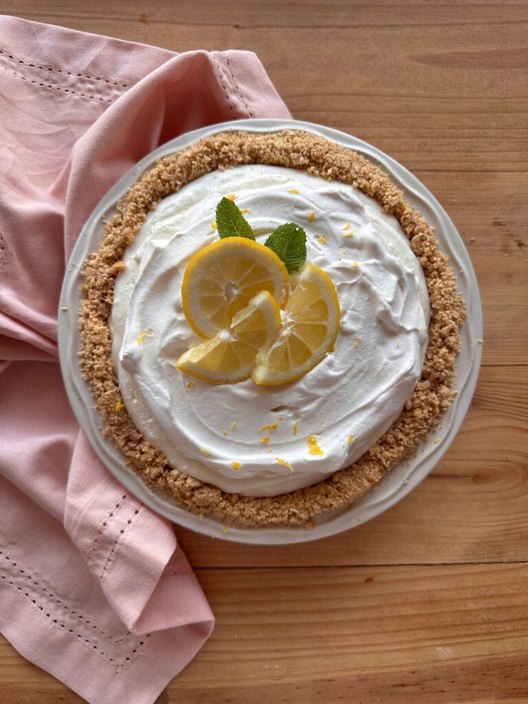 a creamy no bake lemon pie is nestled in a graham cracker crust and garnished with lemon slices