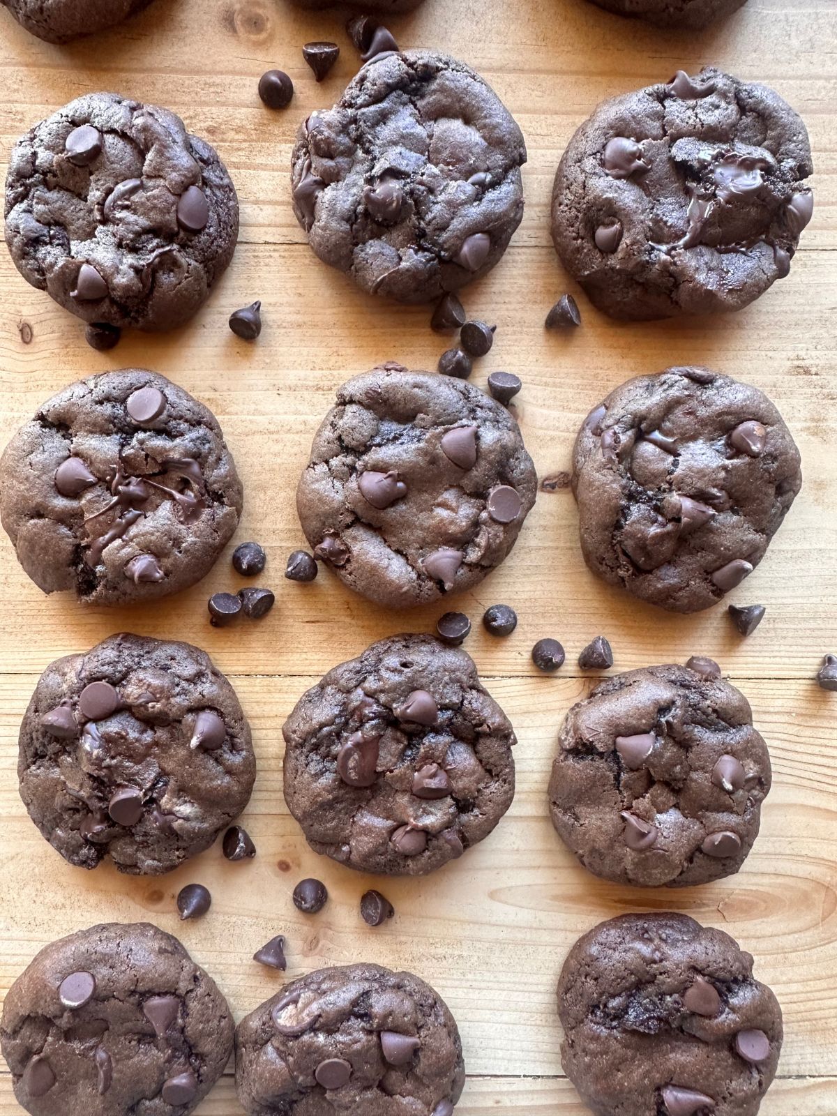 baked chocolate cookies on a wooden surface, with chocolate chips sprinkled around the baked cookies