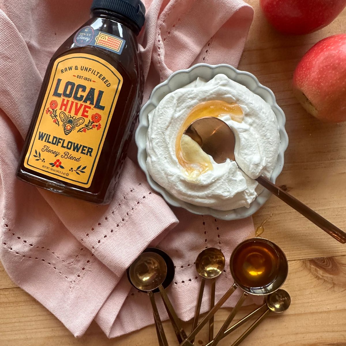 a small bowl of homemade honey whipped cream is center in the photo, with a spoon inserted into the middle. A bottle of honey lays to the side