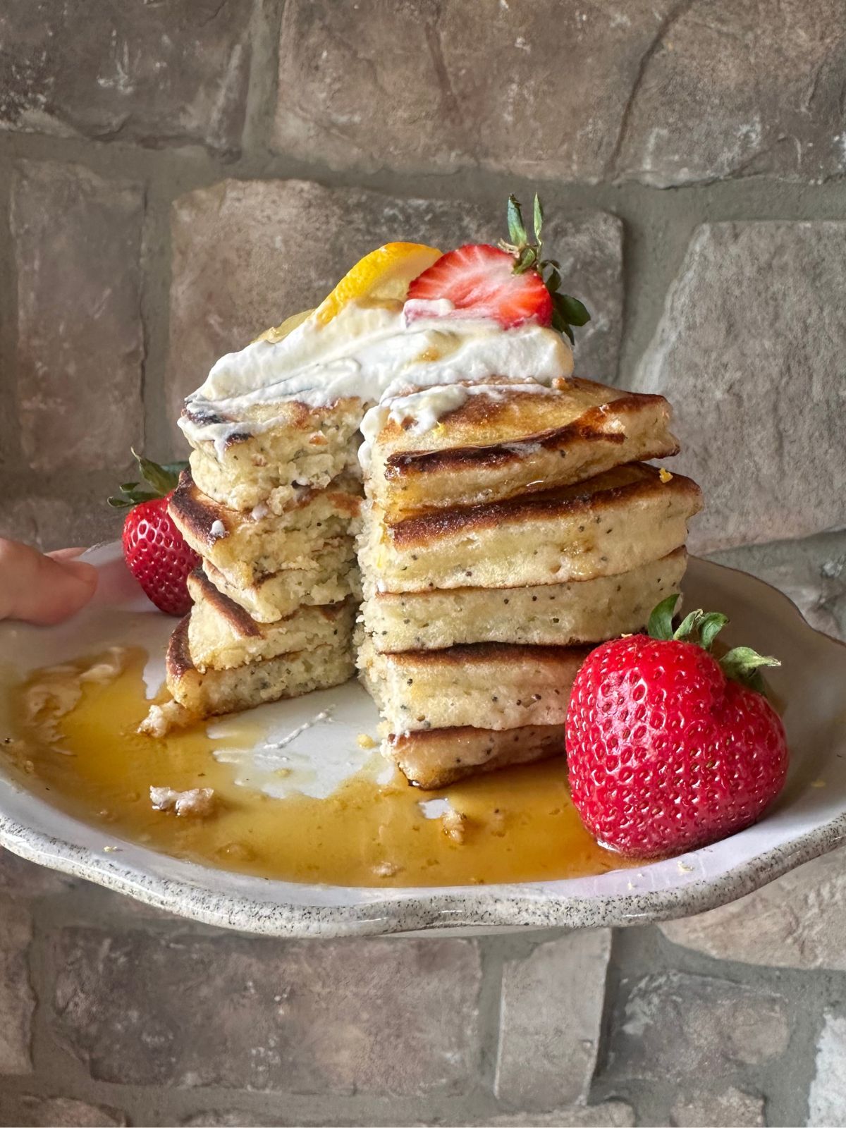 a stack of lemon poppyseed pancakes garnished with maple syrup, whipped cream, and fresh strawberries