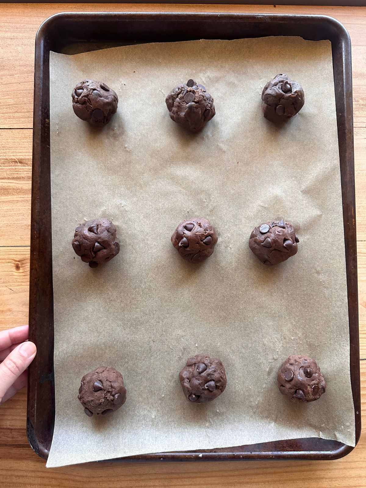 unbaked balls of sourdough chocolate cookies arranged in a row on a baking sheet