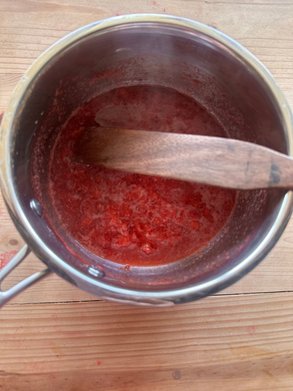 cooked strawberry sauce in a small saucepan. A wooden spoon is stirring the sauce