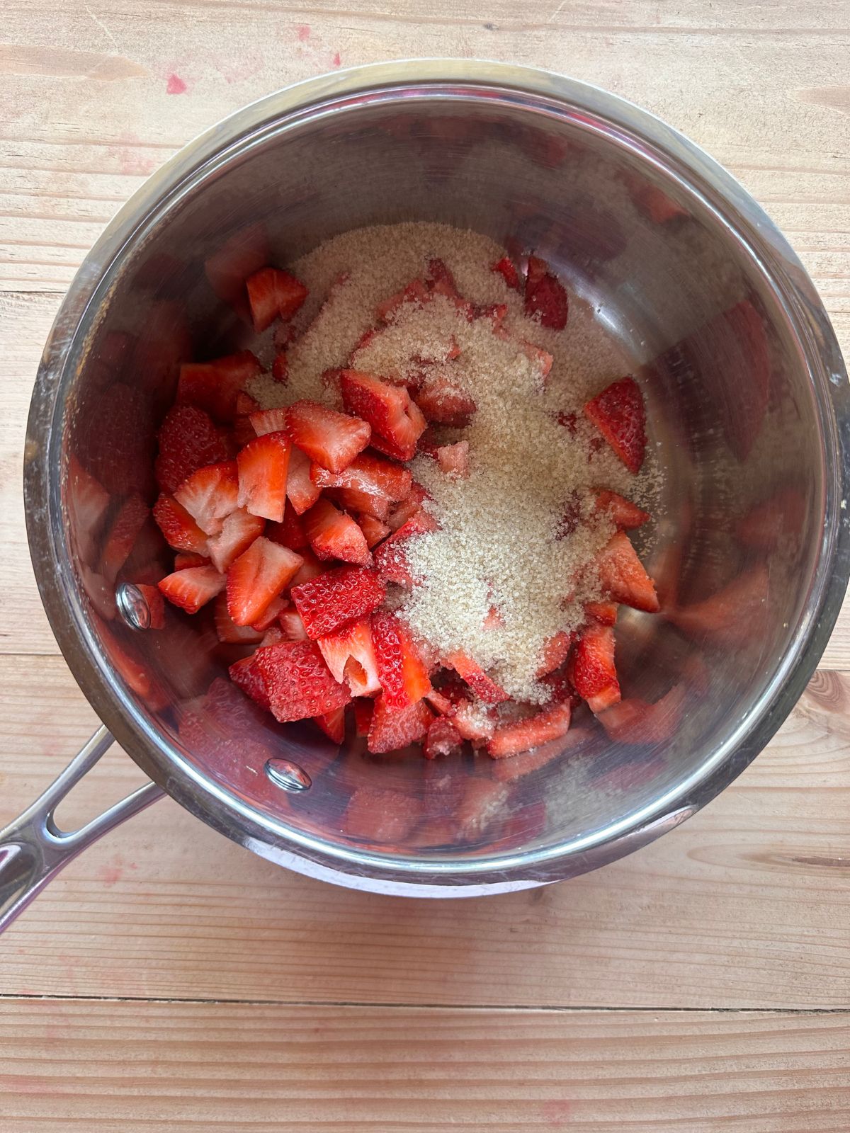chopped strawberries and sugar in a small saucepan, sitting on a wooden countertop