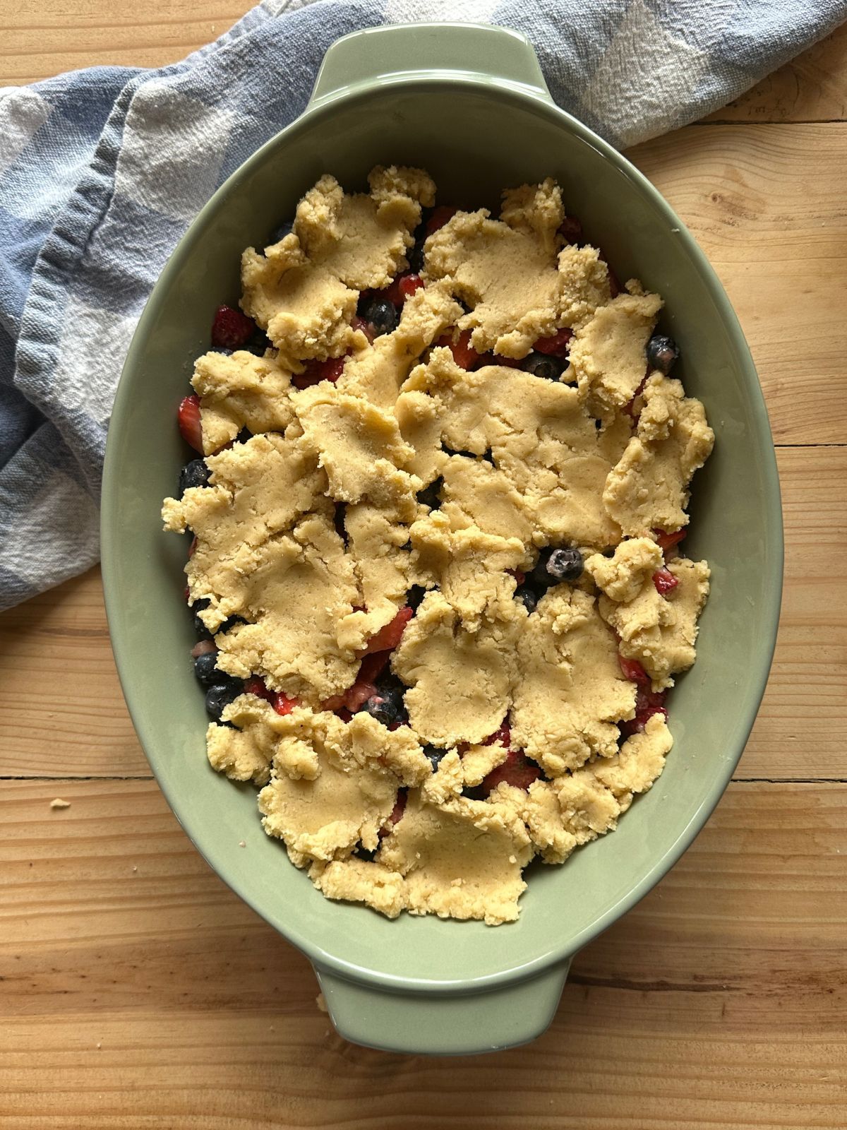 a baking dish on a wooden countertop, filled with berries and topped with sugar cookie dough
