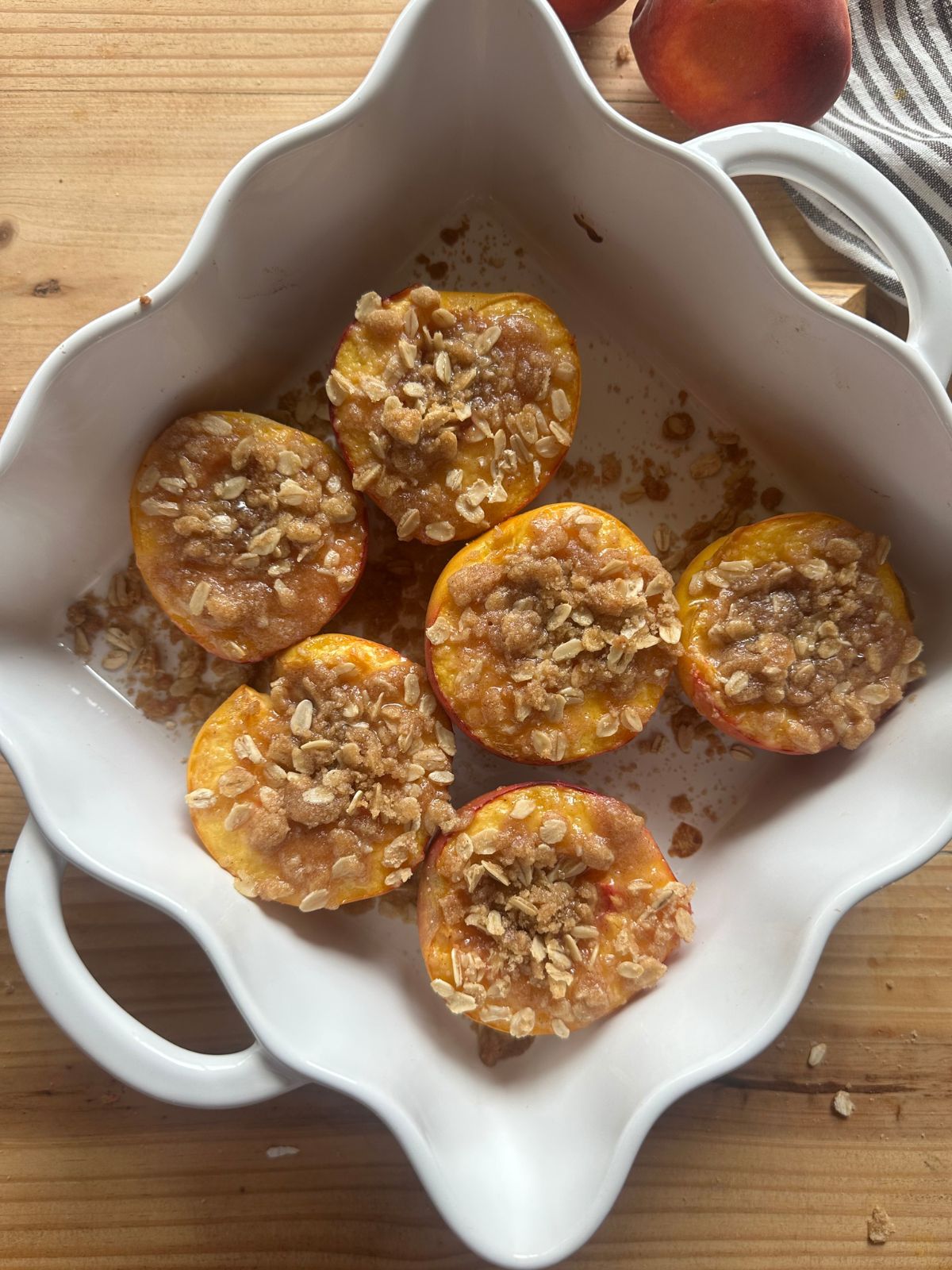 sliced peaches are arranged in a white baking dish and topped with an oatmeal crumble topping