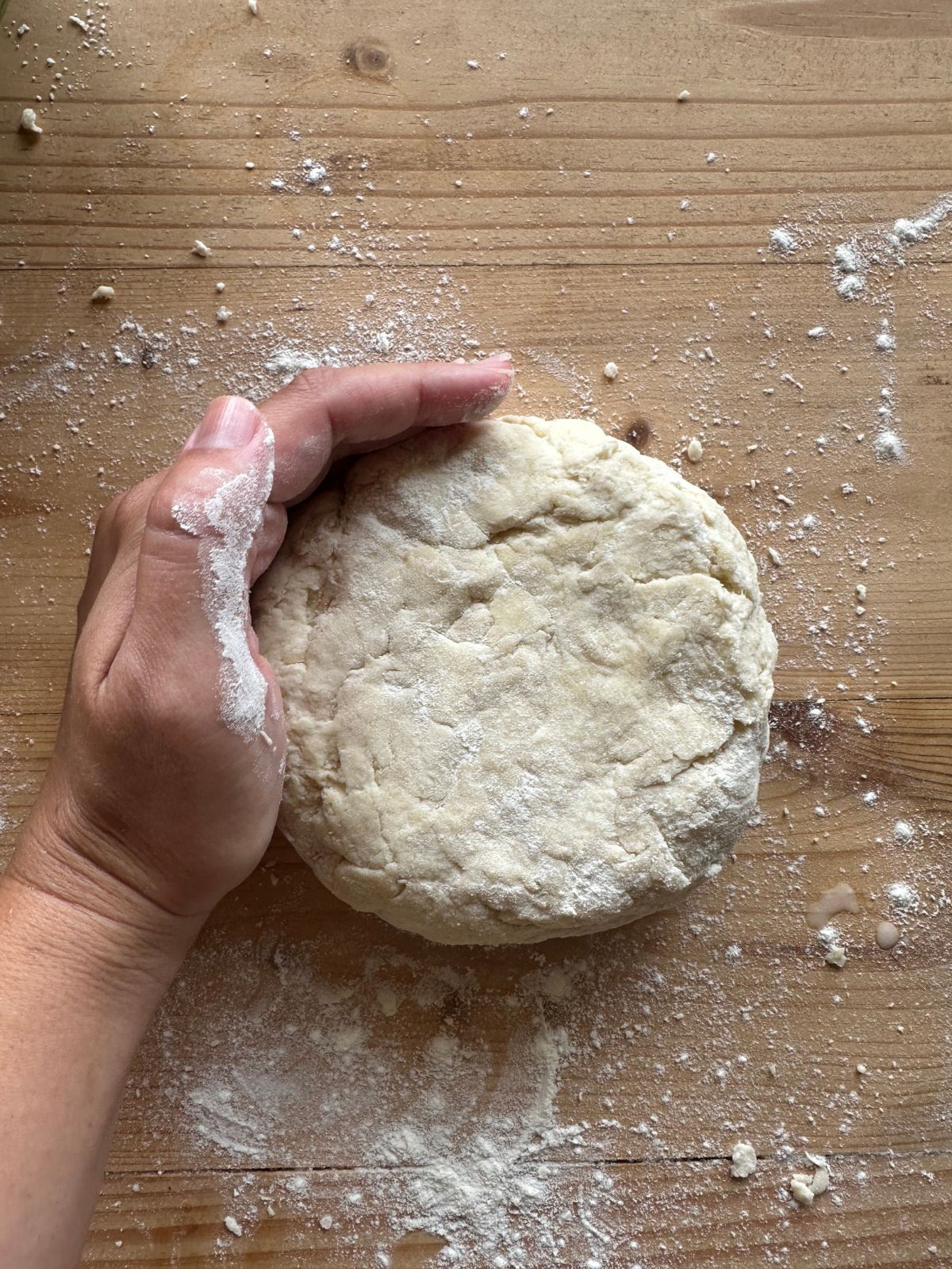 a small disc of sourdough pie crust on a wooden surface. A hand is cupped around the outside edge of the disc