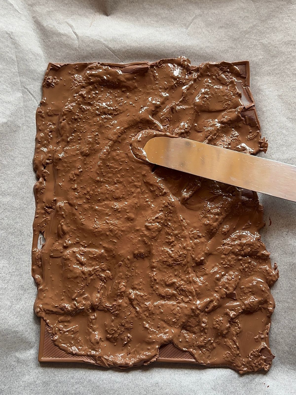 melted chocolate bars on a sheet pan. The melted chocolate is being swirled around by an offset spatula