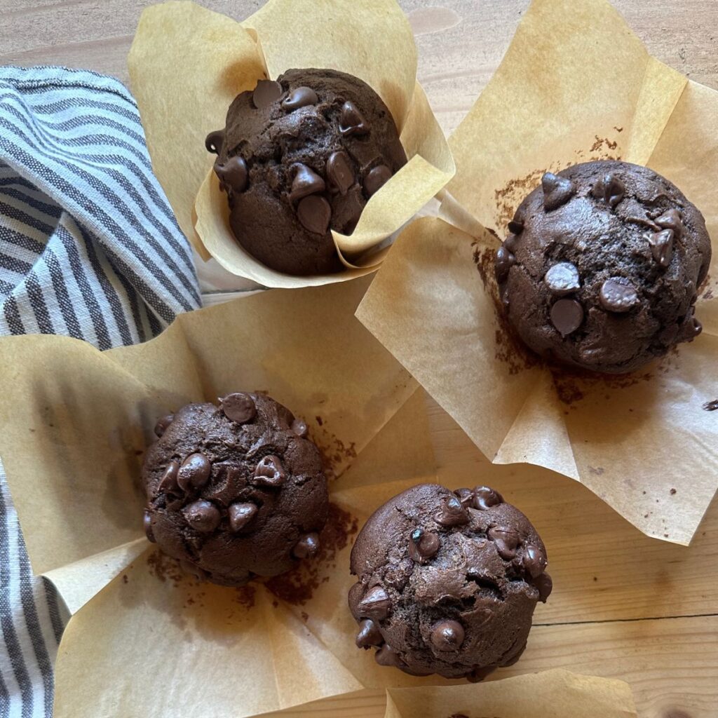 baked chocolate zucchini muffins are arranged on a wooden countertop