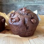 close up image of a sourdough chocolate zucchini muffin, sitting on a wooden countertop