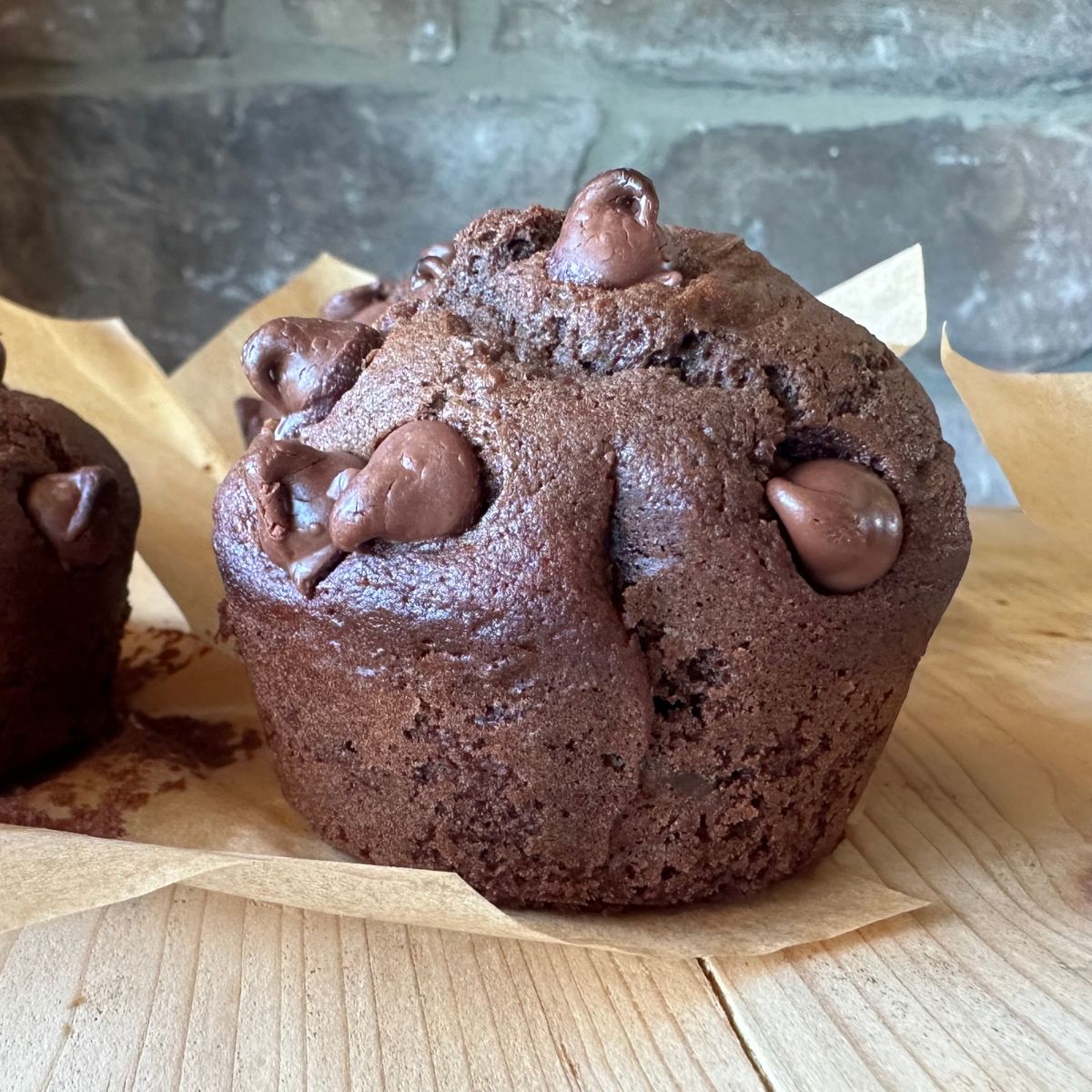 close up image of a sourdough chocolate zucchini muffin, sitting on a wooden countertop