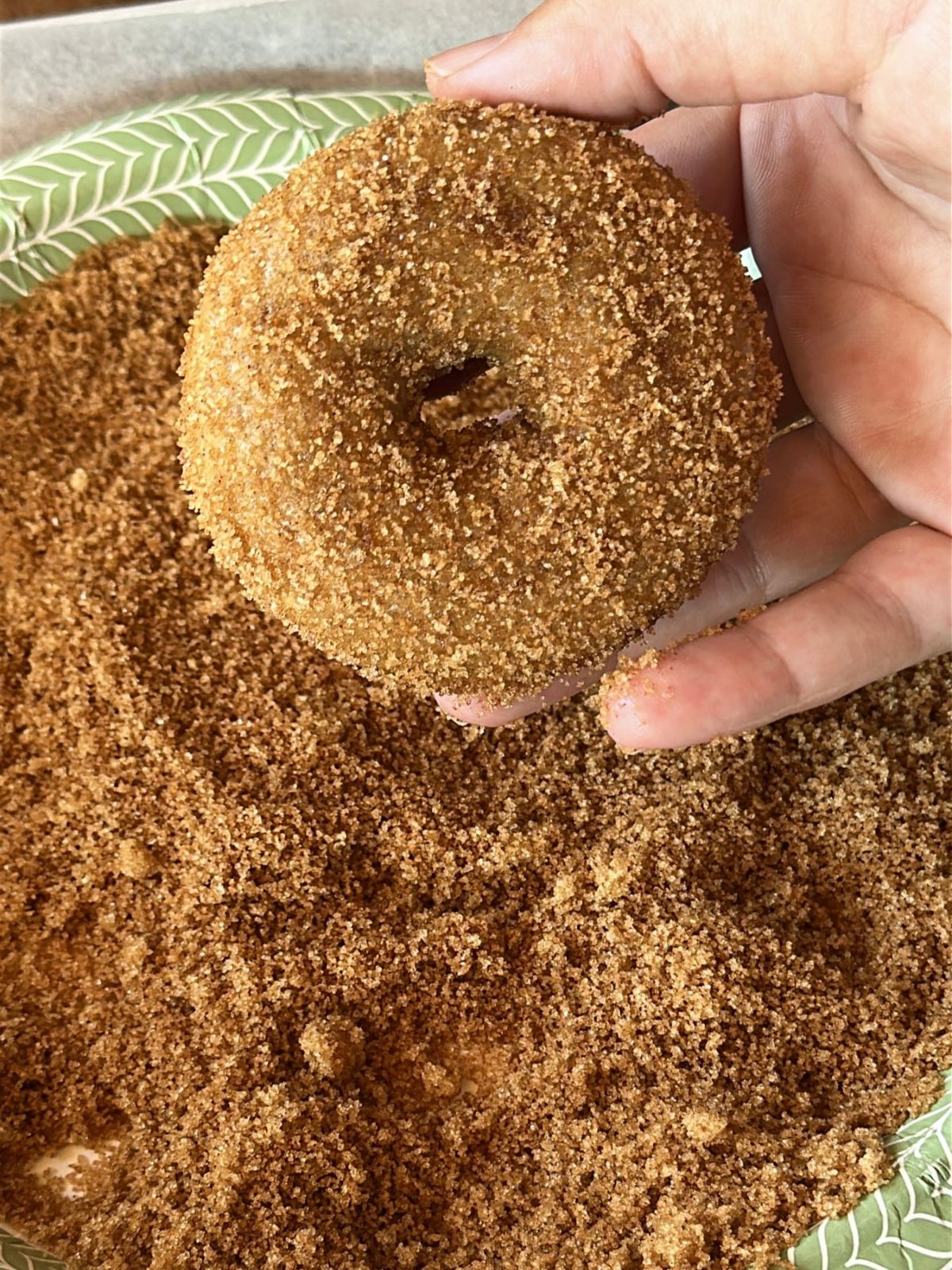 baked apple cider donut being rolled in a cinnamon sugar coating