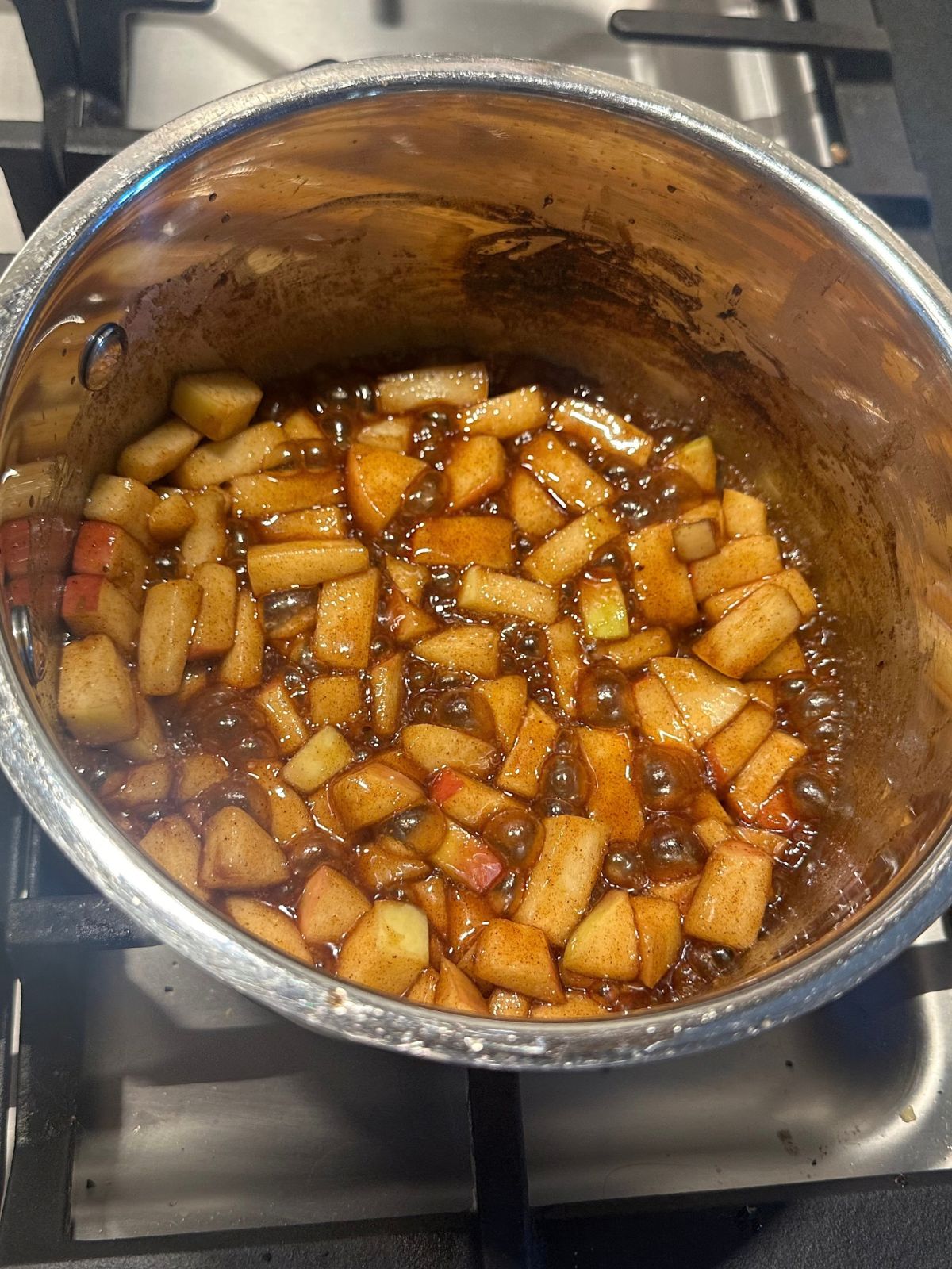 chopped apples cooking in a saucepan with various spices and maple syrup