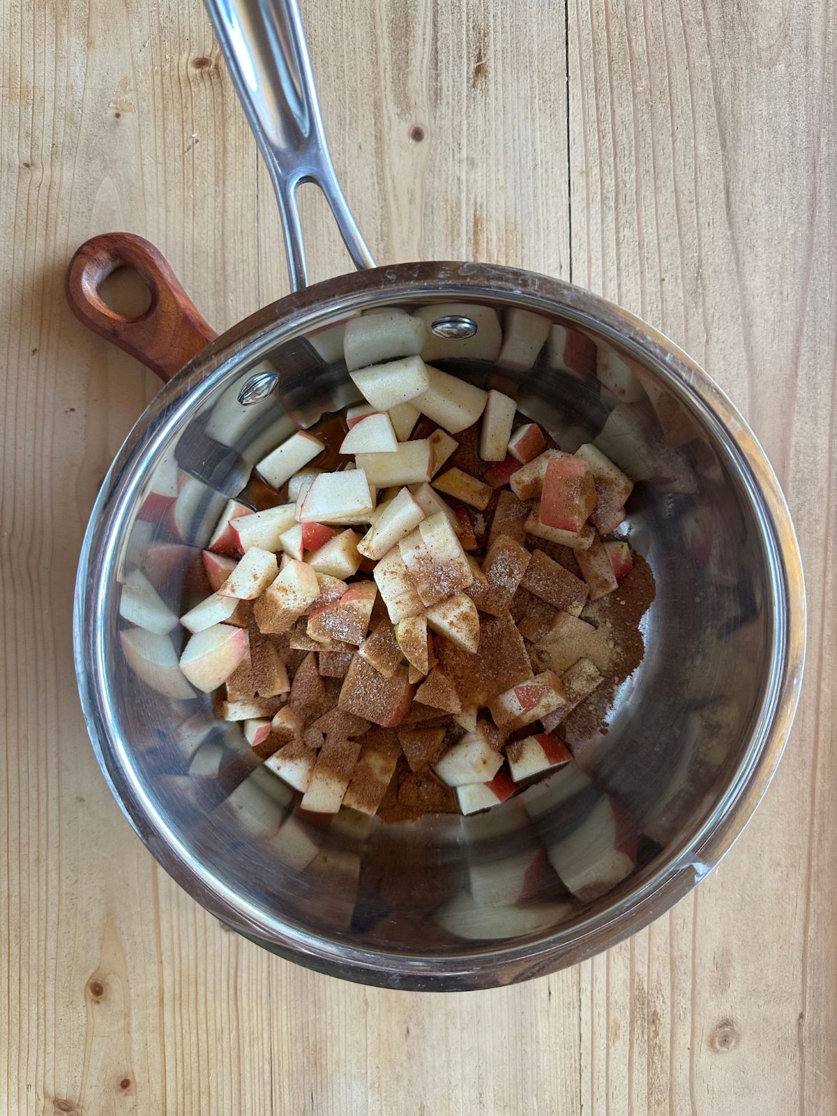 a saucepan with chopped apples, spices, and maple syrup sitting on a wooden countertop